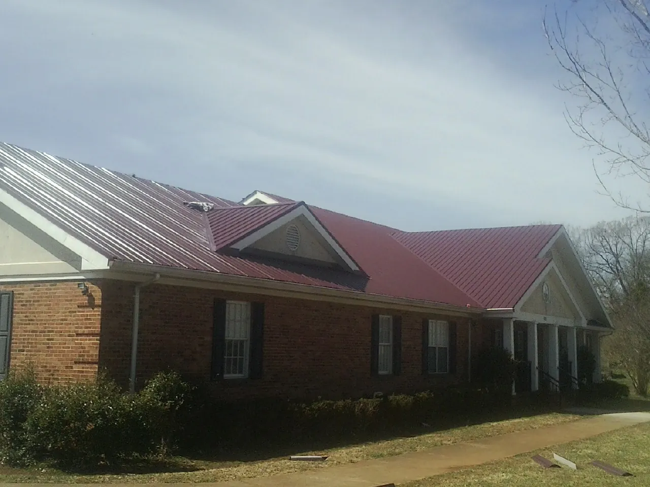 Red metal roof with gabled entries on a long brick building, from a Hail Damage Roof Repair job in Keene