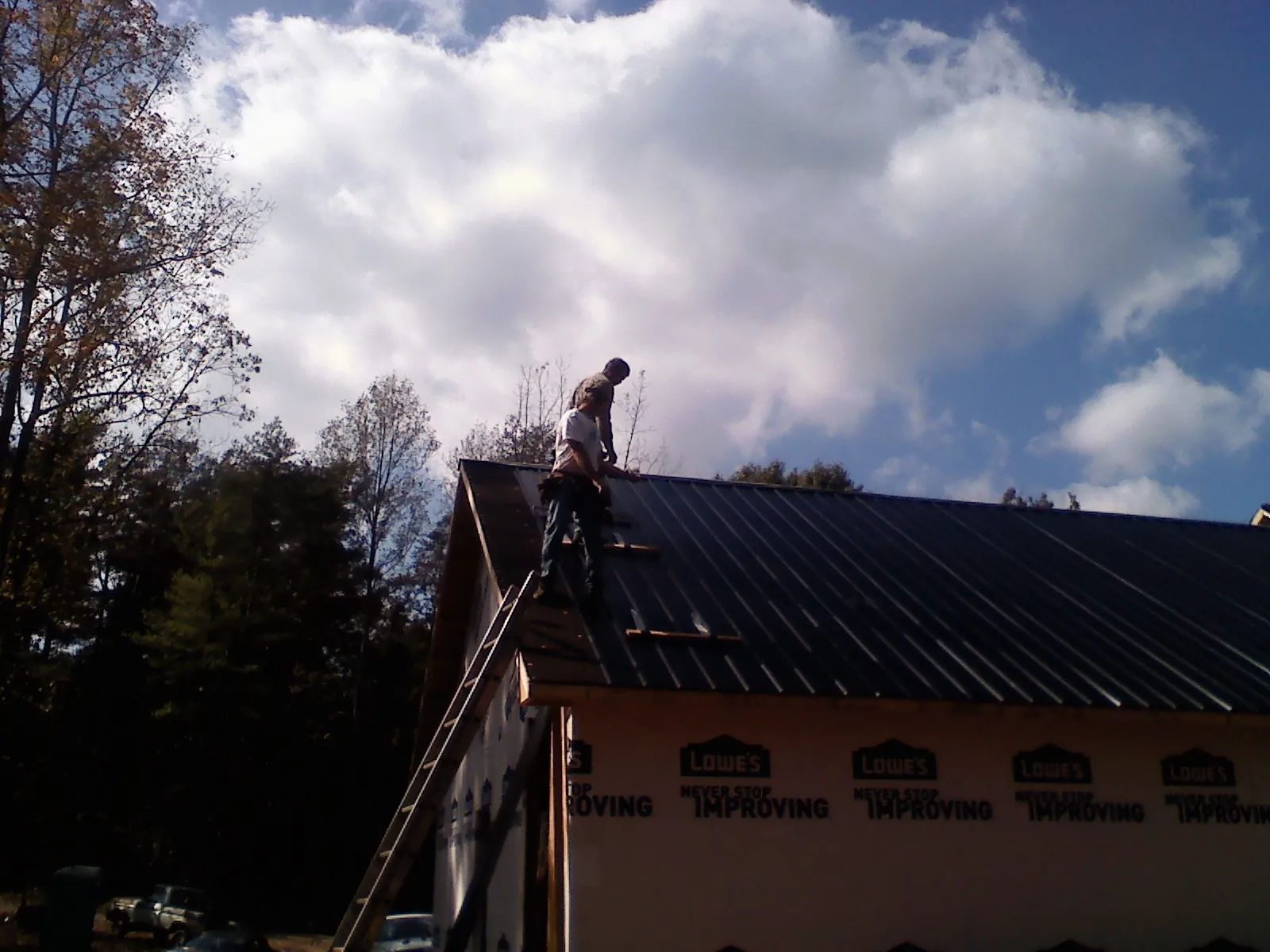 Roofer fastening dark metal panels high against a cloudy sky, from a Roof Inspection job in Keene